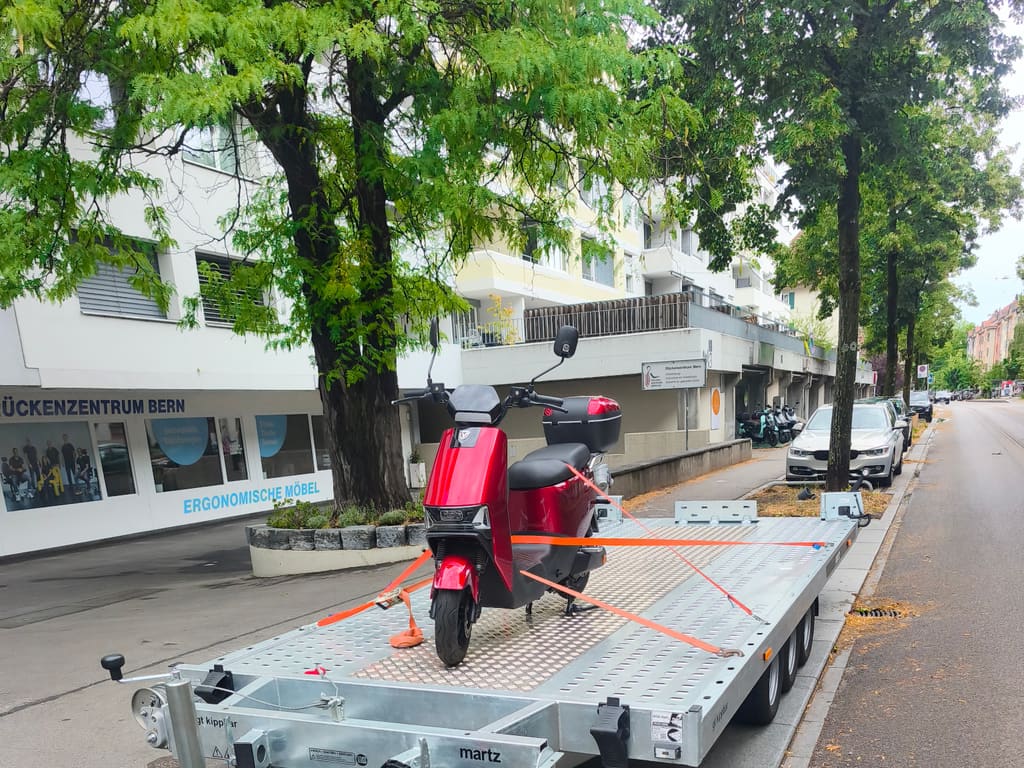 Roter Elektroroller mit Zurrgurten über Kreuz auf dem Anhänger von SWISS Abschleppservice an einer Strasse in Bern